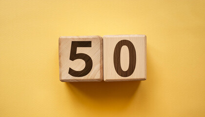 Wooden cubes with number 50 on isolated yellow backdrop. Wood blocks. Close-up. Flat lay