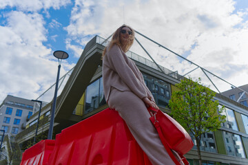 The image depicts a person sitting on a red structure, their face obscured. They hold a red bag...