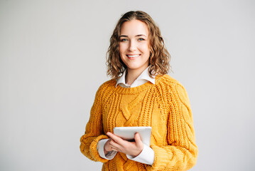 A cheerful businesswoman or student standing isolated on white, holding a digital tablet. Ideal for promoting online education, e-learning platforms, and modern digital technology concepts.