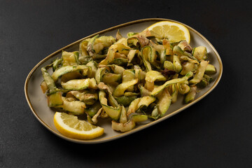 Fried zucchini with lemon on plate on black background.