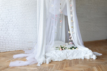 Bed with flowing curtains and garland flowers levitating, hanging flowers. Bedroom interior design.White Mattress for sleeping on the wooden floor with white linens in modern minimalist bright bedroom © stock_studio
