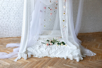 Bed with flowing curtains and garland flowers levitating, hanging flowers. Bedroom interior design.White Mattress for sleeping on the wooden floor with white linens in modern minimalist bright bedroom © stock_studio