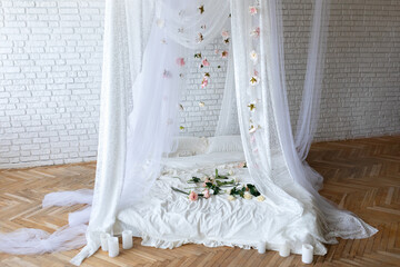 Bed with flowing curtains and garland flowers levitating, hanging flowers. Bedroom interior design.White Mattress for sleeping on the wooden floor with white linens in modern minimalist bright bedroom © stock_studio