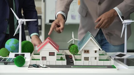 Two Asian businessmen in formal suits discuss ideas and suggestions at an office desk, focusing on green housing estates, city planning, renewable energy, and achieving net zero emissions by 2050.