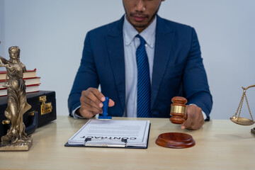 An Asian businessman in a formal suit works alone at a lawyer's desk, by golden scales, law books,...