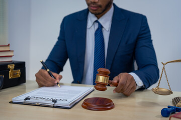 An Asian businessman in a formal suit works alone at a lawyer's desk, by golden scales, law books,...