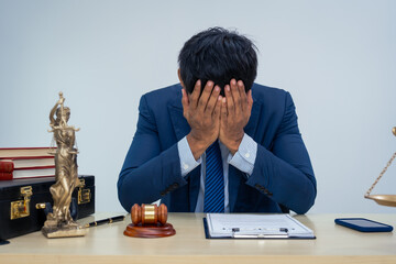 An Asian businessman in a formal suit works alone at a lawyer's desk, by golden scales, law books,...