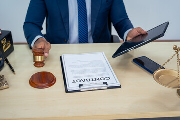 An Asian businessman in a formal suit works alone at a lawyer's desk, by golden scales, law books,...