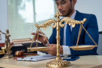 An Asian businessman in a formal suit works alone at a lawyer's desk, by golden scales, law books, leather bags, and a Lady Justice statue, emphasizing personal freedom and legal empowerment.