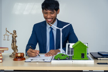 An Asian businessman in a formal suit works alone at a lawyer's desk, with golden scales, law...