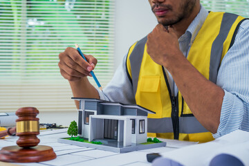 Asian architect works at a desk with house blueprints, checking plans on a laptop and clipboard,...