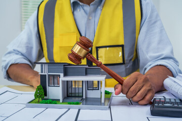 Asian architect works at a desk with house blueprints, checking plans on a laptop and clipboard,...
