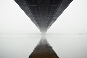 Under the bridge in a fog. Bridge over a river - symmetric view from below. Bridge disappearing in a dense fog.