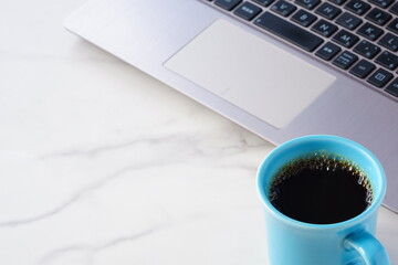 コーヒーを飲みながらノートパソコンでデスクワークをしているイメージ
