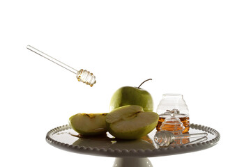 Honey dripping from glass stick on green apples on a white plate with jar of honey. White background. Rosh Hashanah greeting card (Jewish New Year holiday) concept.