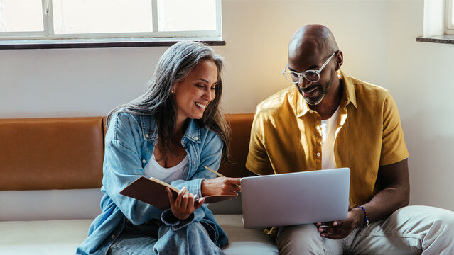 Modern team collaboration with mature black man and woman sitting, discussing over a laptop