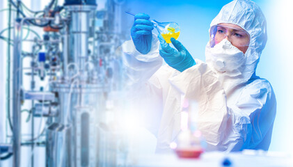 Woman biologist. Scientist examines test tube. Bioreactor near laboratory assistant. Scientist with flask in hands. Biologist in protective suit and glasses. Experiments in biology.