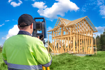 Man builder. Surveyor back to camera. Geodetic instrument in front of worker. Surveyor near house under construction. Man uses optical theodolite. Geodetic surveys. Surveyor supervises construction