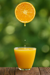 glass of orange juice with splash and falling drops on table with green garden on the background