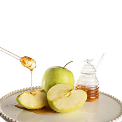 Honey dripping from glass stick on green apples on a white plate with jar of honey. White background. Rosh Hashanah greeting card (Jewish New Year holiday) concept.