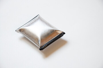 A telephone battery that is swollen from overheating lies on a white background, the phone battery