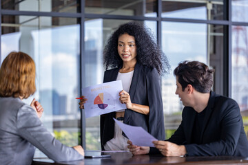 Young African woman sale manager is showing annual report chart to her colleagues in the executive meeting for next year plan with market share pie chart for global business and investment