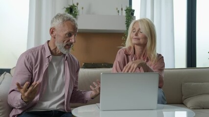 Pensive serious married elderly 50s Caucasian couple senior mature woman female male man talk dispute debate discussing business couch. Husband wife quarrel online video call laptop home family argue