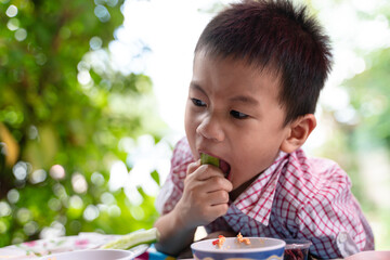 3 years old Thai Boy eating fresh cucumber with Thai spicy chili paste.