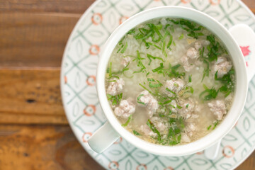 A bowl of rice soup with minced pork and herbs.