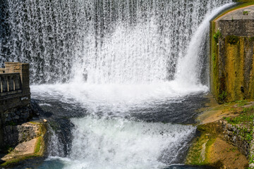 The beautiful artificial waterfall and tourists on a sunny summer day.
