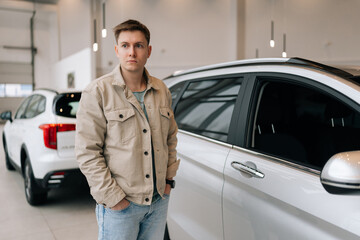 Portrait of male visitor walking in modern auto showroom and choosing new vehicle to buy or rent. Handsome young man buyer dreaming buy vehicle at dealership. Concept of buying new auto at showroom