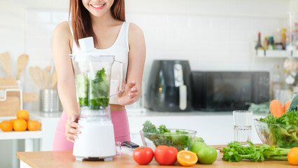 Attractive sporty young woman making vegetable smoothie with blender in kitchen. Healthy lifestyle and dieting concept.