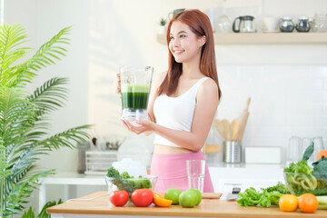 Smiling young sporty woman using a blender to making green smoothie in the kitchen. Healthy eating and dieting concept.