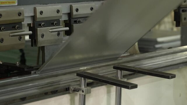 The employee hands are not bending the large parts of the metal on the bending machine, closeup. The CNC operator bending a metal product bends.