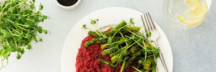 Beetroot risotto with rice and sesame seeds, baked asparagus with pea microgreens, banner