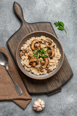 Risotto with brown champignons in a bowl on a wooden cutting board. Italian food. Top view, flat lay, vertical.