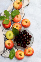 Ripe red apples and cherries in a bowl on a light background. Selective focus.
