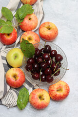 Ripe red apples and cherries in a bowl on a light background. Selective focus.