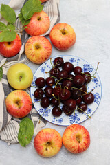 Ripe red apples and cherries in a bowl on a light background. Selective focus.