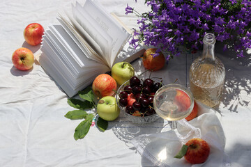 Picnic table with wine, apples, cherry and flowers in the summer garden. Beautiful composition of...