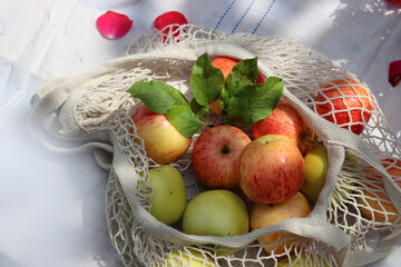 Green and red apples with leaves in white cotton mech bag. Eco friendly reusable shopping bag close up photo. Ripe apples in a string bag on a white tablecloth. Eating healthy concept. 