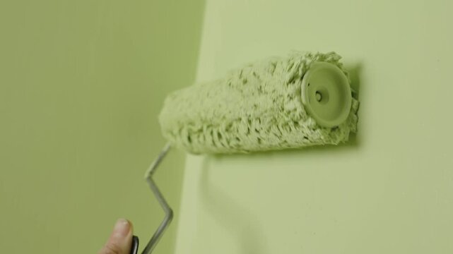 A young woman painter paints the wall green with a roller. New renovation of your apartment
