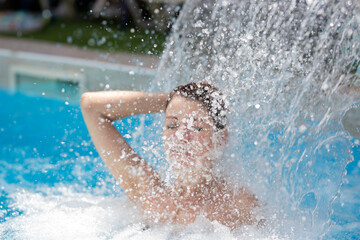 A woman enjoys relaxing in a swimming pool under the jets of water.