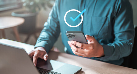 technology, application, device, app, smartphone, marketing, social, multimedia, touch, media. A man is holding a cell phone and sitting at a desk with a laptop. The man is focused on his work.