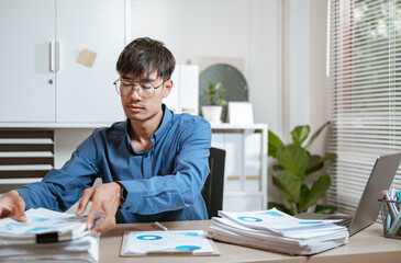 document, executive, job, manager, occupation, paperwork, stress, stressed, working, problem. A man is sitting at a desk with a pile of papers in front of him and he is focused on the papers.