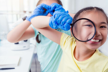 Naklejka premium Joyful young girl hold magnifying glass up to her face, smiling widely in playful moment Another child playfully interact in background showcasing fun curiosity of scientific discovery in a classroom 