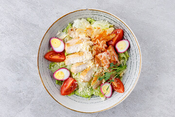 Caesar salad with chicken and bacon on a gray background on a plate for a restaurant menu