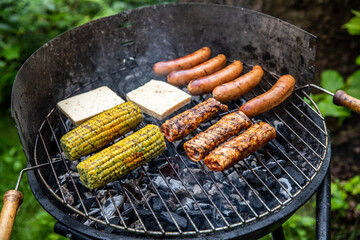 Ein Holzkohlegrill mit Würstchen Maiskolben und Grillkäse belegt.