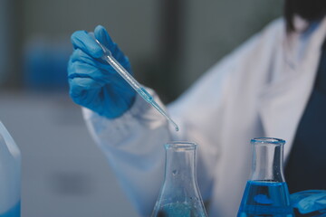 Group of dedicated scientist conduct chemical experiment in medical laboratory, carefully drop precise amount of liquid from pipette into test tube for vaccine drug or antibiotic development. Neoteric