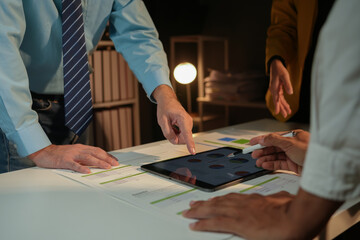 Late night business team using digital tablet and stylus to analyze financial data and highlight...